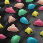 Zoom sur les picots multicolores du tapis de réflexologie pour massage des pieds, galets en plastique rose bleu vert jaune sur fond noir
